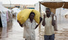 Displaced Sudanese men look on as they carry sacks through a flooded street near the UNHCR tents, following a heavy rainfall.